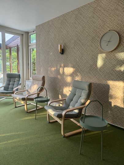 Ein stilvoller Raum mit gemütlichen Stühlen und grünem Teppichboden. Das Licht fällt sanft durch die Fenster und sorgt für eine einladende Atmosphäre.