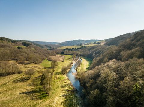 Eine malerische Landschaft mit sanften Hügeln und einem klaren Fluss. Die Bäume sind noch ohne Blätter, und der Himmel ist strahlend blau.