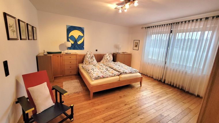 Ein modernes Schlafzimmer mit einem Doppelbett und Holzfußboden. Große Fenster lassen viel Tageslicht herein.