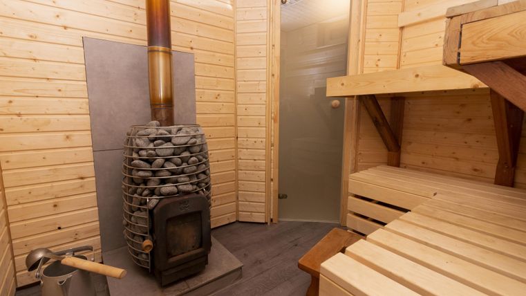 Une sauna confortable avec un revêtement en bois et un poêle en pierre. Les bancs sont en bois clair et la pièce dégage de la chaleur.