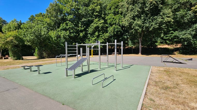 Une zone d'entraînement en plein air avec différents équipements de fitness. Entourée d'arbres et de pelouses, elle crée une atmosphère accueillante.