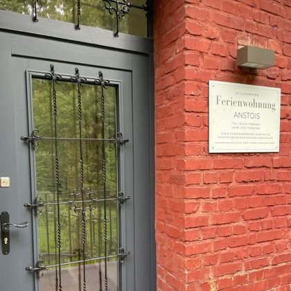 Une porte d'entrée d'un appartement de vacances avec un look moderne. Les murs sont en brique rouge et un panneau avec le nom est bien visible.