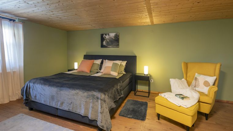 Een gezellig slaapkamer met een groot bed en zachte kleuren. Een gele fauteuil en zacht licht creëren een uitnodigende sfeer.