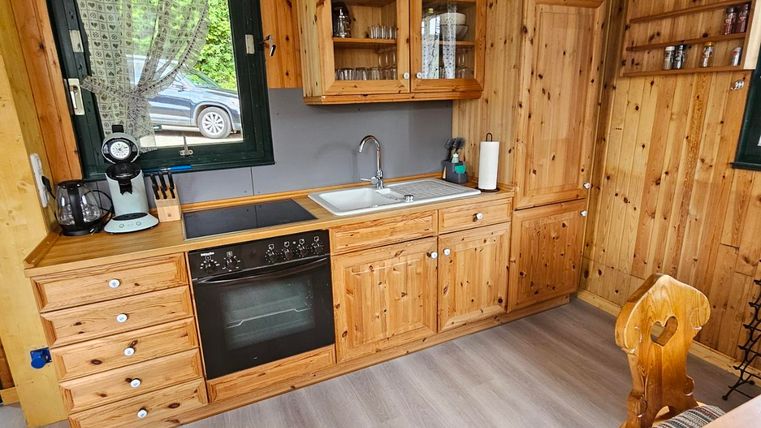 A cozy wooden kitchen with modern furnishings. The floor is light, and the windows provide plenty of light.