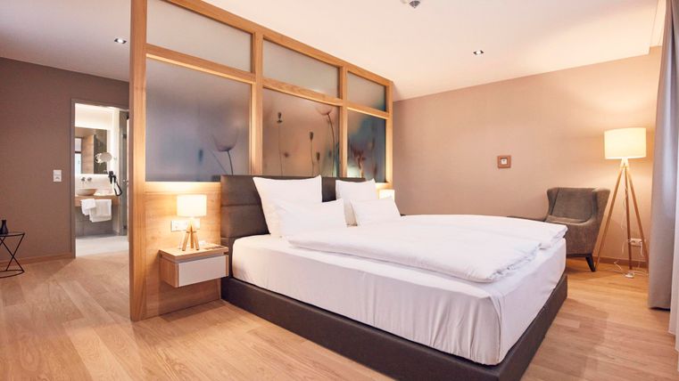 Een moderne slaapkamer met een groot tweepersoonsbed en elegante nachtkastjes. De warme kleurstelling en de houten vloer creëren een gezellige sfeer.