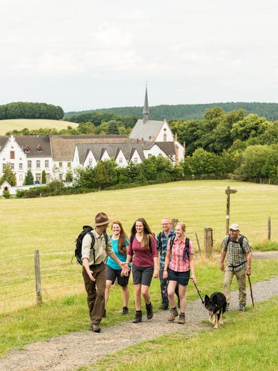 A ranger leads a group. In the background, you can see the Mariawald monastery.
