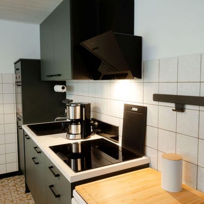 A modern kitchen with black cabinets and a bright countertop. The stove and the hood are elegantly integrated.