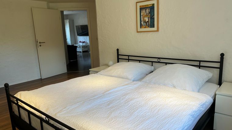 Ein gemütliches Schlafzimmer mit einem großen Doppelbett und weißen Bettdecken. Im Hintergrund ist eine Tür zu einem weiteren Raum zu sehen.