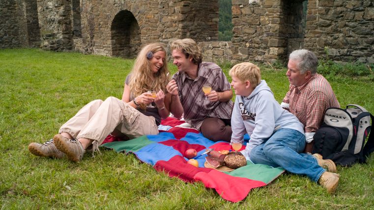 Quatre personnes font un pique-nique sur une couverture colorée devant un vieux mur de pierre.