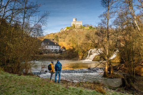 Deux personnes se tiennent au bord de l'Elzbach avec vue sur le moulin de Pyrmont et le château de Pyrmont.