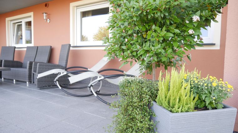 Een gezellige buitenruimte met uitzicht op een terras. Er zijn comfortabele stoelen, planten en een mooi vormgegeven bloembak.