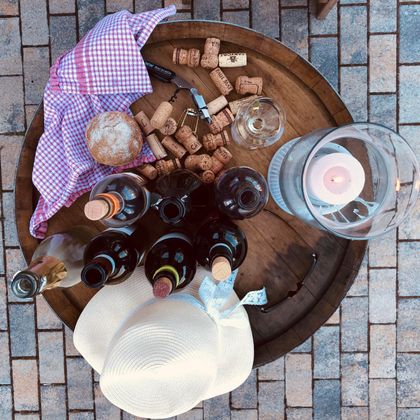 Een rustieke tafel met verschillende wijnflessen, glazen en korken. Daarnaast liggen een hoedje en een doek in een informele sfeer.