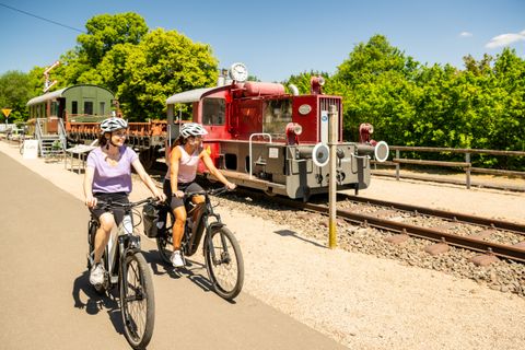 Deux cyclistes passent devant une vieille locomotive sur une piste cyclable.