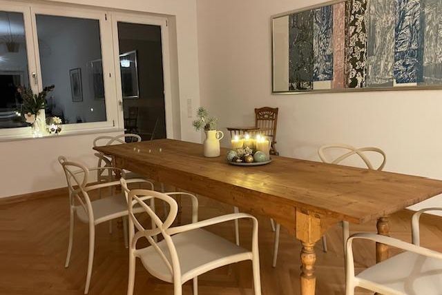 Ein esszimmer mit einem großen Holztisch und weißen Stühlen. Auf dem Tisch sind Kerzen und eine dekorative Schale.