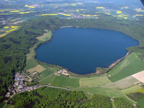Een grote, ovale meer omgeven door groene bossen en velden. In de buurt is een klein dorp te zien.