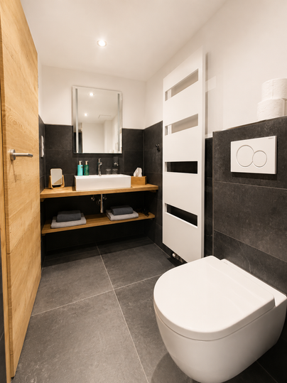 Een moderne badkamer met donkere tegels en licht hout. Het heeft een wastafel met spiegel en een toilet.