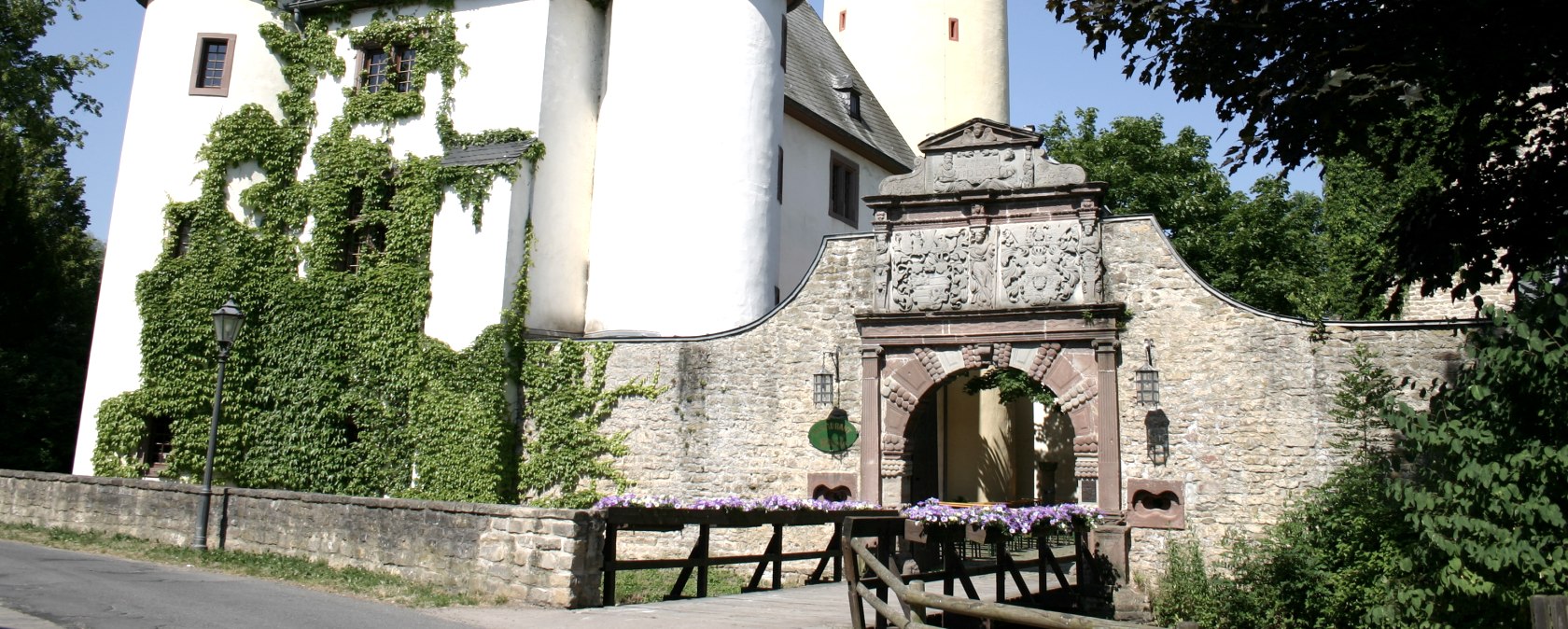 Burg Rittersdorf mit zwei runden Türmen und einem hohen, gelben Turm. Ein Torbogen mit Verzierungen führt in die Burg. Efeu wächst an den Wänden., © Frank Schaal