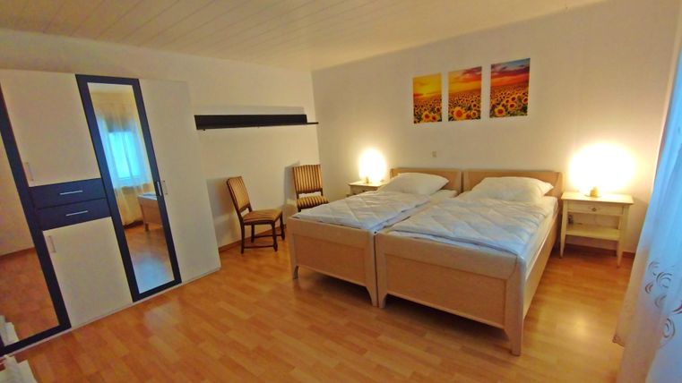 Une chambre confortable avec deux lits simples et une lumière chaude. Des images de tournesols sont accrochées au mur, et il y a un miroir ainsi qu'une chaise.