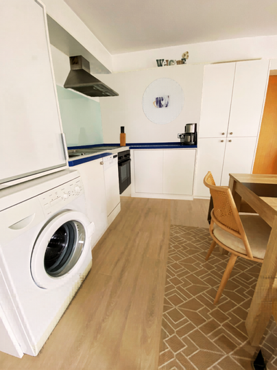 Une cuisine moderne avec une machine à laver, une cuisinière et une table à manger. Le sol a un motif attrayant et les murs sont clairs.