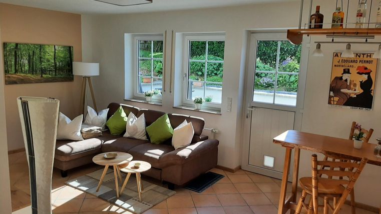 Ein helles Wohnzimmer mit einem bequemen Sofa und einem kleinen Tisch. Große Fenster lassen viel Licht herein und bieten einen Blick auf den Garten.