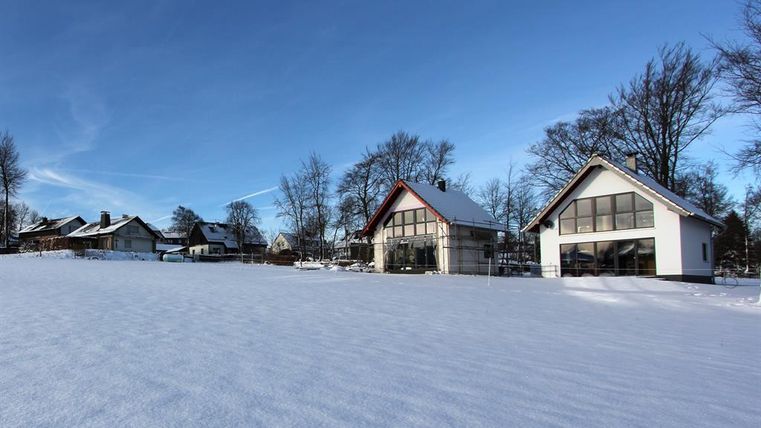 A snowy landscape with two modern houses. In the background, more buildings and a clear blue sky are visible.