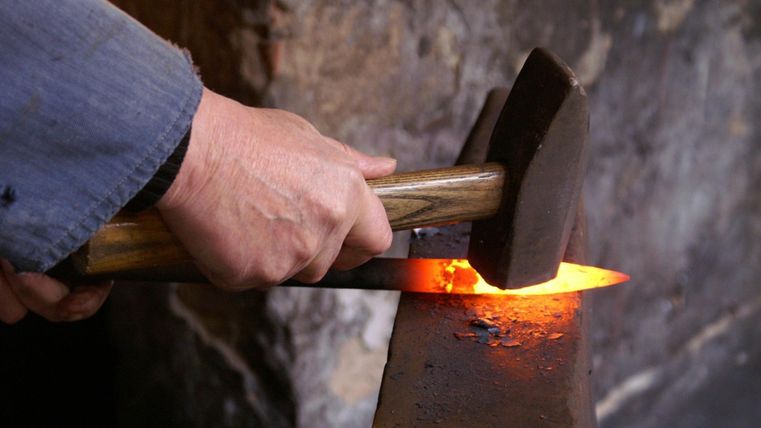 Een smid bewerkt een gloeiend stuk metaal met een hamer op een aambeeld.