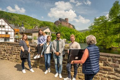 Eine GRuppe von Personen, die eine Stadtführung machen, im Hintergrund ist eine Burg zu sehen