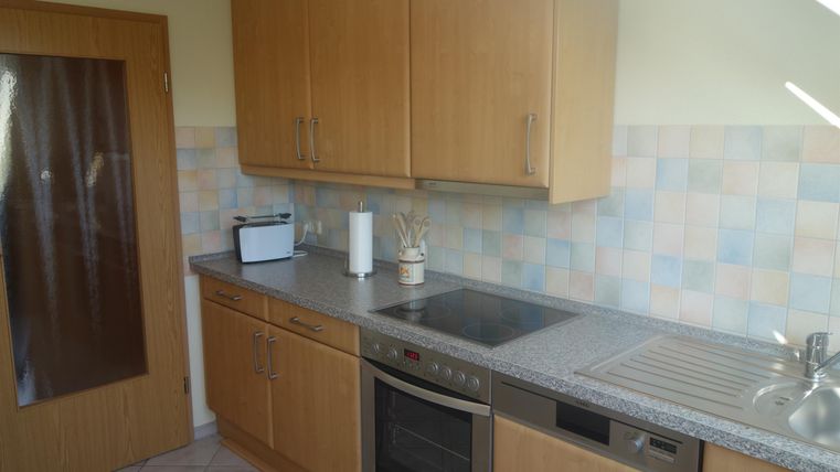 A modern kitchen with wooden cabinets and a bright, friendly atmosphere. The workspace is well organized and features various household appliances.