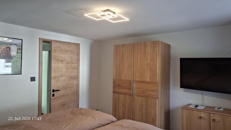 A modern bedroom with a double bed, a wooden wardrobe, and a television. On the wall, there is a door and a decorative picture.