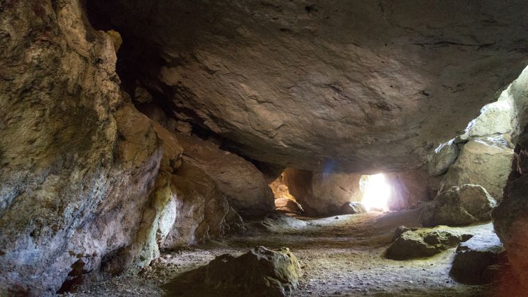 Interior view of the Kakus Cave with rock formations and a ray of light at the end.