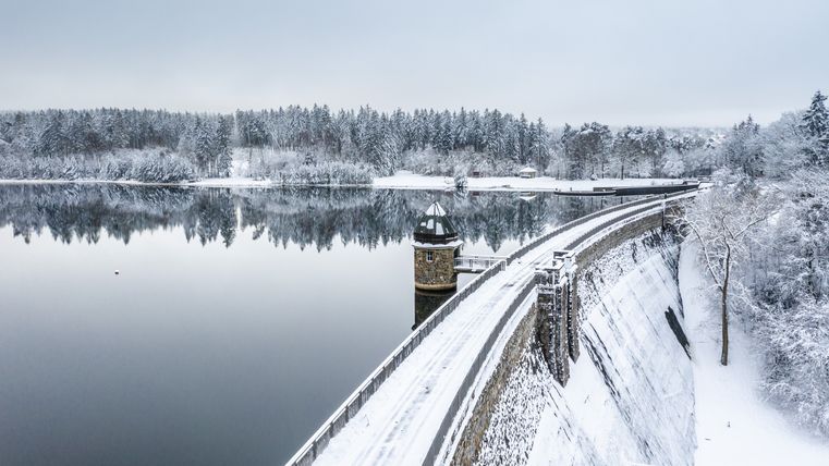 Barrage hivernal du Dreilägerbach avec un paysage enneigé et une eau calme.