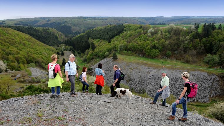 Eine Wandergruppe steht am Aussichtspunkt im Kaulenbachtal und blickt von einem Schieferhügel herunter ins Kaulenbachtal.