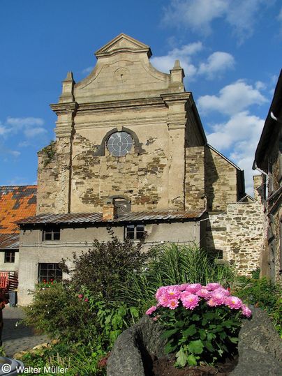 Une tour d'observation en pierre se dresse entre de grands arbres. Le ciel est clair et bleu, et les environs semblent calmes et préservés.