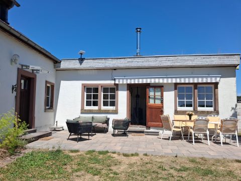 Une maison confortable avec une terrasse et un jardin. Le ciel est clair et bleu, idéal pour des journées détendues en plein air.