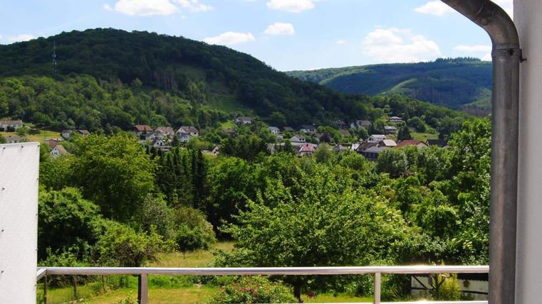 A picturesque view of green hills and a small village. The sky is blue with some white clouds.
