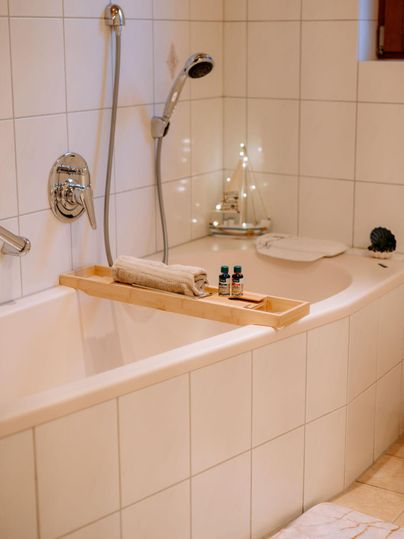 A modern bathroom with a bathtub and wooden elements. On the bathtub shelf, there is a towel and some essential oils.