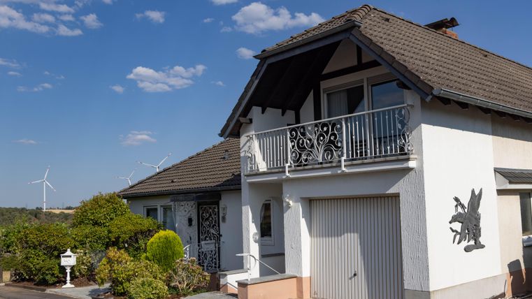 A charming house with a balcony and a beautiful facade. In the background, wind turbines and a blue sky can be seen.
