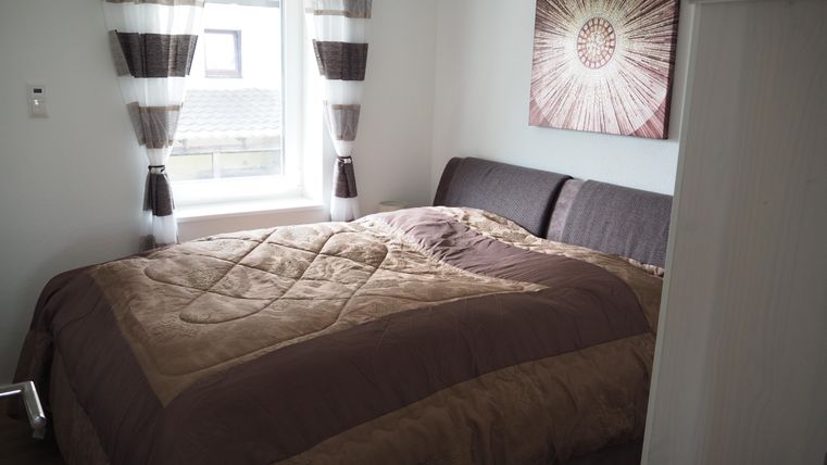 Ein gemütliches Schlafzimmer mit einem großen Bett und einem modernen Wandbild. Helle Vorhänge und eine Fensteransicht sorgen für ein einladendes Ambiente.