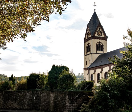 The church of St. Remigius in Oberweis, surrounded by trees and a stone wall, under a cloudy sky., © TI Bitburger Land