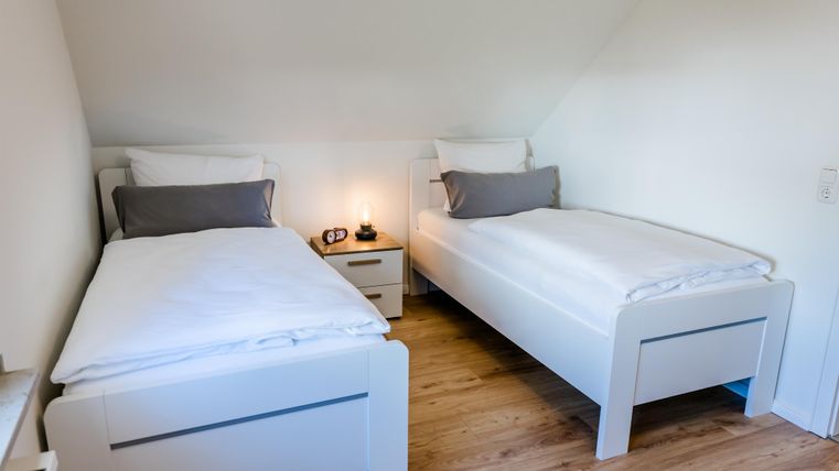 Een moderne slaapkamer met twee eenpersoonsbedden. De houten vloer en de lichte muren creëren een gezellige sfeer.