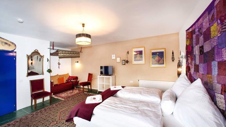 A cozy room with a large bed and a seating area. The walls are colorfully decorated, and there is a rug on the floor.
