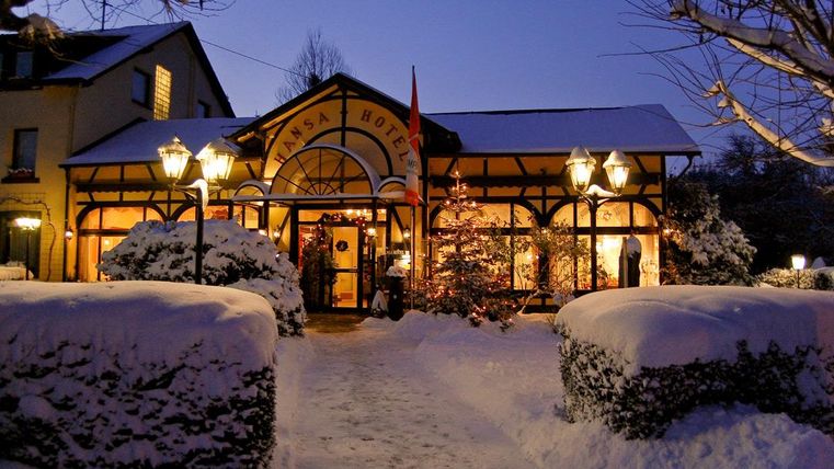 Ein einladendes Hotelgebäude im Schnee bei Dämmerung. Die warmen Lichter und die festliche Dekoration sorgen für eine gemütliche Atmosphäre.
