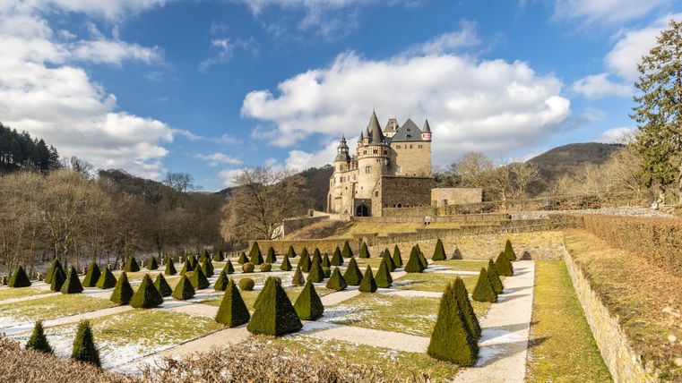 Schloss Bürresheim mit gepflegtem Garten und blauen Himmel im Hintergrund.