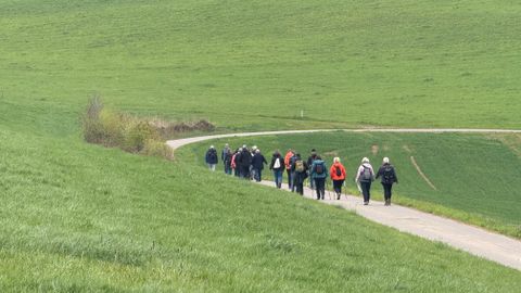 Een uitgestrekt landschap met groene weiden en een heldere blauwe lucht. Op de voorgrond staat een groot kruis.