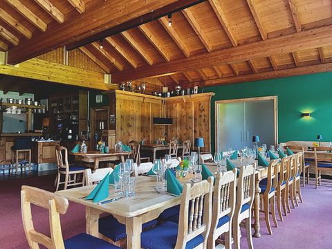 In een ruimte met houten plafond staat een lange houten tafel, die in de kleur groen gedekt is. Op de achtergrond zijn er nog meer gedekte tafels.