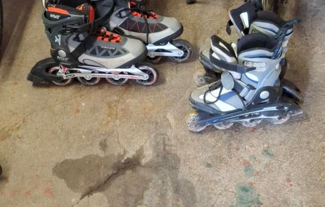 Twee paar inline skates staan op een vloer in een garage. Op de achtergrond zijn fietsen zichtbaar.