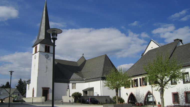 Een kerk met een hoge toren staat naast een modern gebouw. De lucht is blauw en er zijn geen wolken zichtbaar.