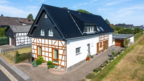 Een modern huis in traditionele vakwerkstijl met een zwart dak. De tuin is netjes en beplant met kleurrijke bloemen.