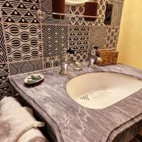 A bathroom with a sink and a decorative tiled wall. On the shelf lie towels and a small bowl.