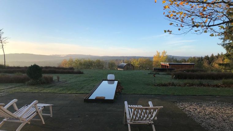 Een rustige terras met twee ligstoelen en een lange, spiegelende waterpartij. Op de achtergrond strekt zich een groene landschap onder een heldere lucht uit.